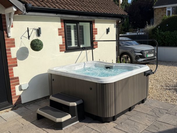 Hot tub with steps, situated next to a house and parking area.