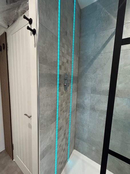 Modern shower with grey tiles and bright blue accent lighting.