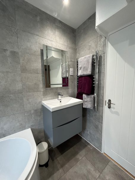Modern bathroom featuring a grey wall, vanity unit, mirror, and towels in a stylish setting.