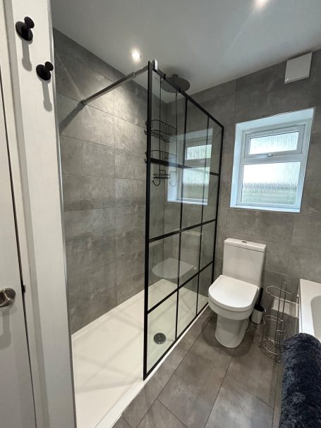 Modern bathroom with a glass shower cubicle and a white toilet. Grey tiled walls.