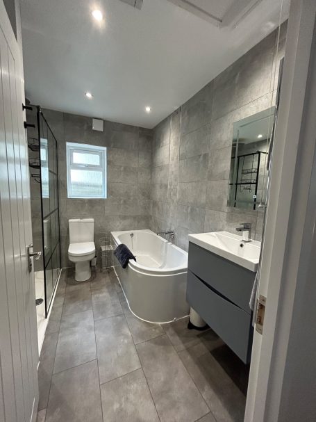 Modern bathroom featuring a shower, bathtub, toilet, and stylish grey decor.