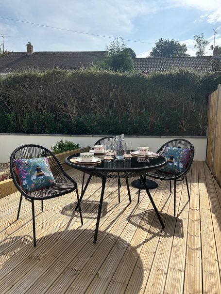 A small outdoor seating area with a round table and four chairs on a wooden deck.
